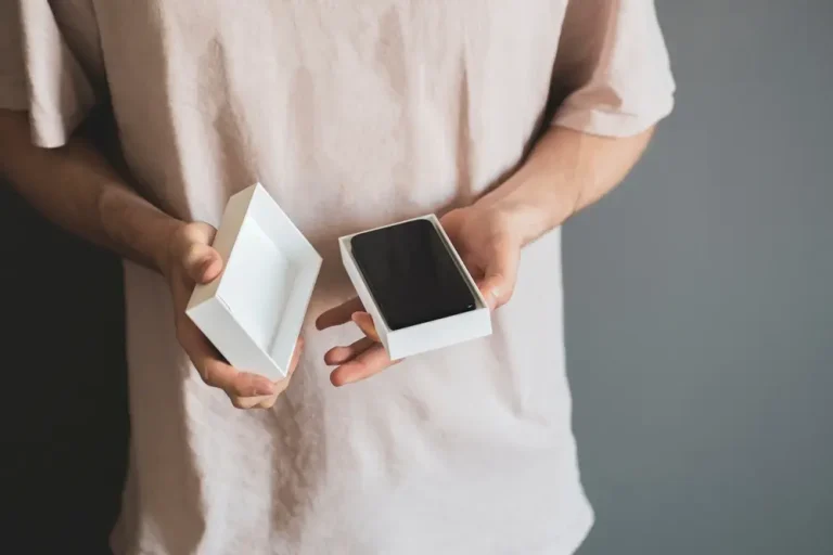 The person is holding the box or casing of a new smartphone and unboxing it.